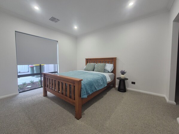 Een slaapkamer met een houten bed, een klein nachtkastje, een kamerplant en uitzicht door een raam.
