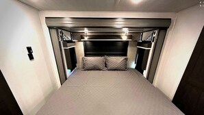 Une petite pièce étroite et fermée, comprenant un lit, deux petites tables et une tête de lit dotée de lampes.