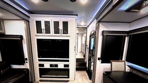 Un espace de vie compact comprenant un meuble de rangement intégré pour les appareils multimédias, un coin salon et une kitchenette.