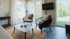 Ett modernt vardagsrum med en soffa, två fåtöljer, ett soffbord, en tv och stora fönster med gardiner.