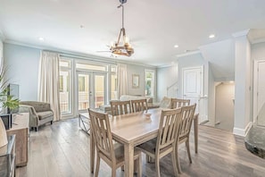 A spacious dining area with a wooden table and chairs, a chandelier, and large windows with curtains. - Spacious 4BR - Sleeps 10 - Walk to Beach - 7401 (Myrtle Beach)