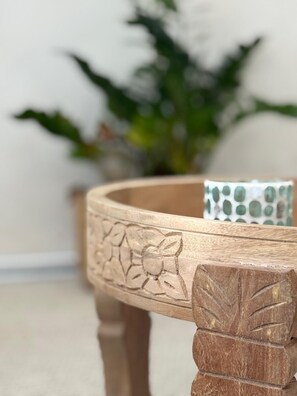 A wooden table with carved floral patterns, a white vase with green leaves, and a white wall in the background. - Casa mar y sol (Insel Poel)