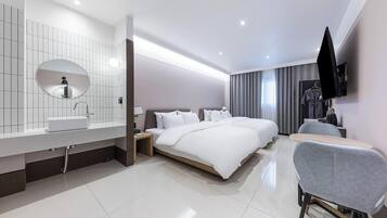 Una habitación de hotel moderna con una cama grande, una zona de estar separada, un baño con espejo y lavamanos, y un televisor de pantalla plana montado en la pared.