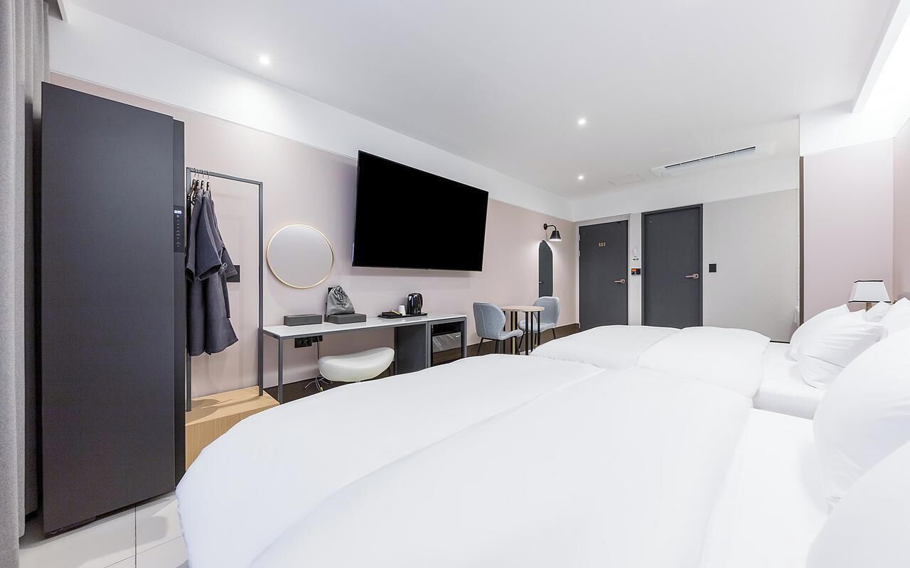 A modern hotel room with a large bed, a desk with a chair, a television, and a wardrobe.