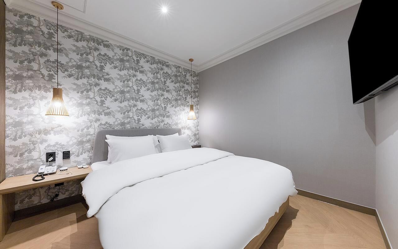 A modern hotel room with a large bed, two bedside tables, a wall-mounted TV, and a patterned wallpaper.