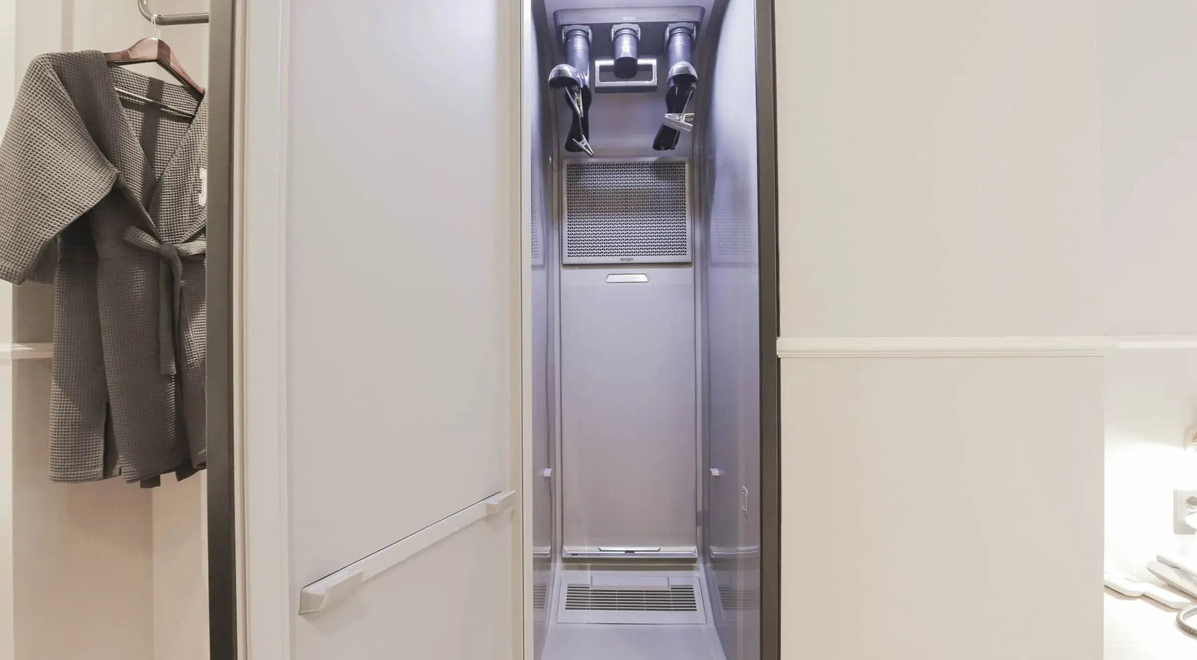 Un ascensor metálico estrecho con dispensador de agua y una rejilla de ventilación.