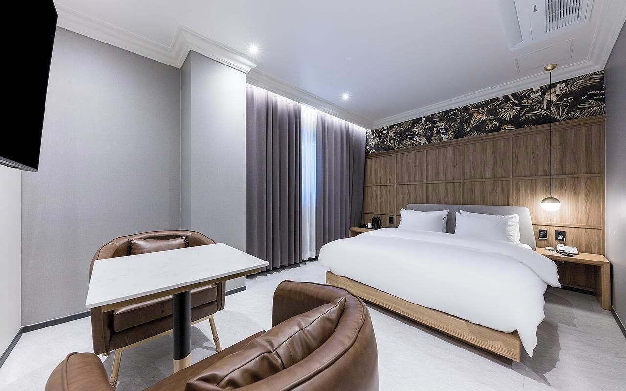 A modern hotel room with a large bed, a desk, a chair, and a nightstand.