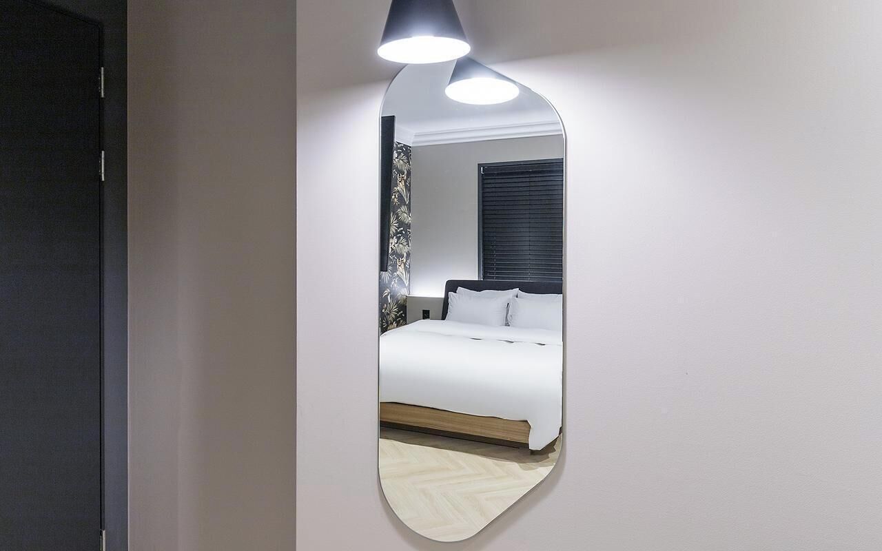 Een slaapkamer met een bed, een spiegel en een plafondlamp.