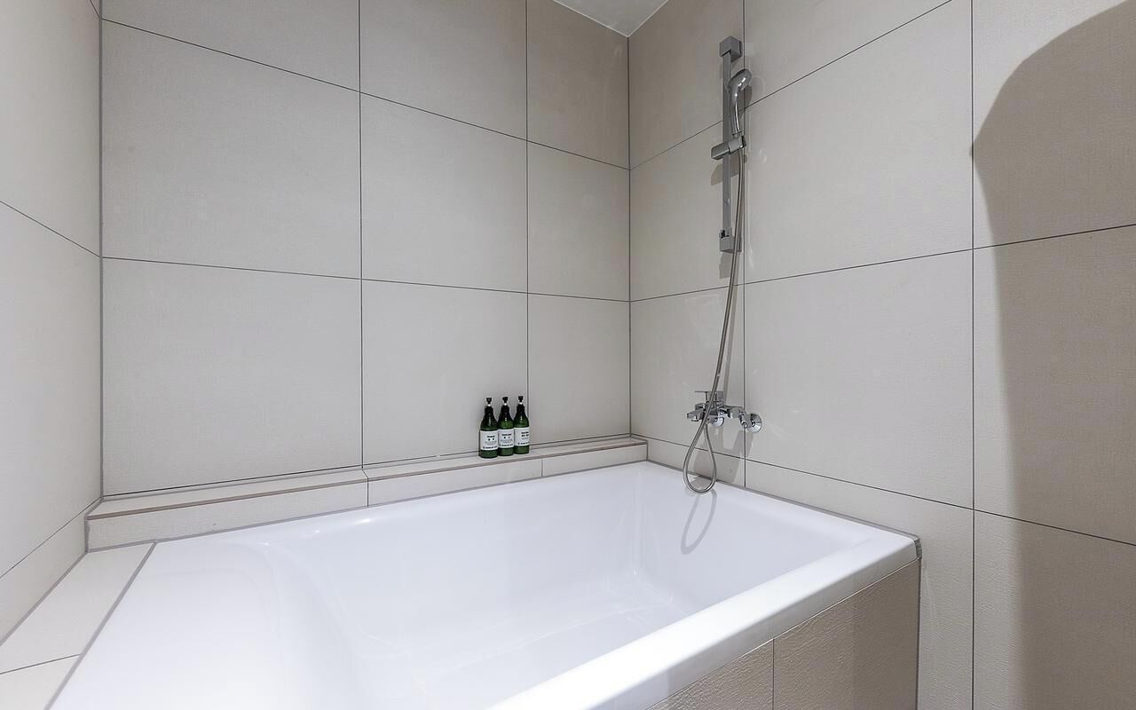 A modern bathroom with a white bathtub, a showerhead, and two bottles of shampoo on the wall.