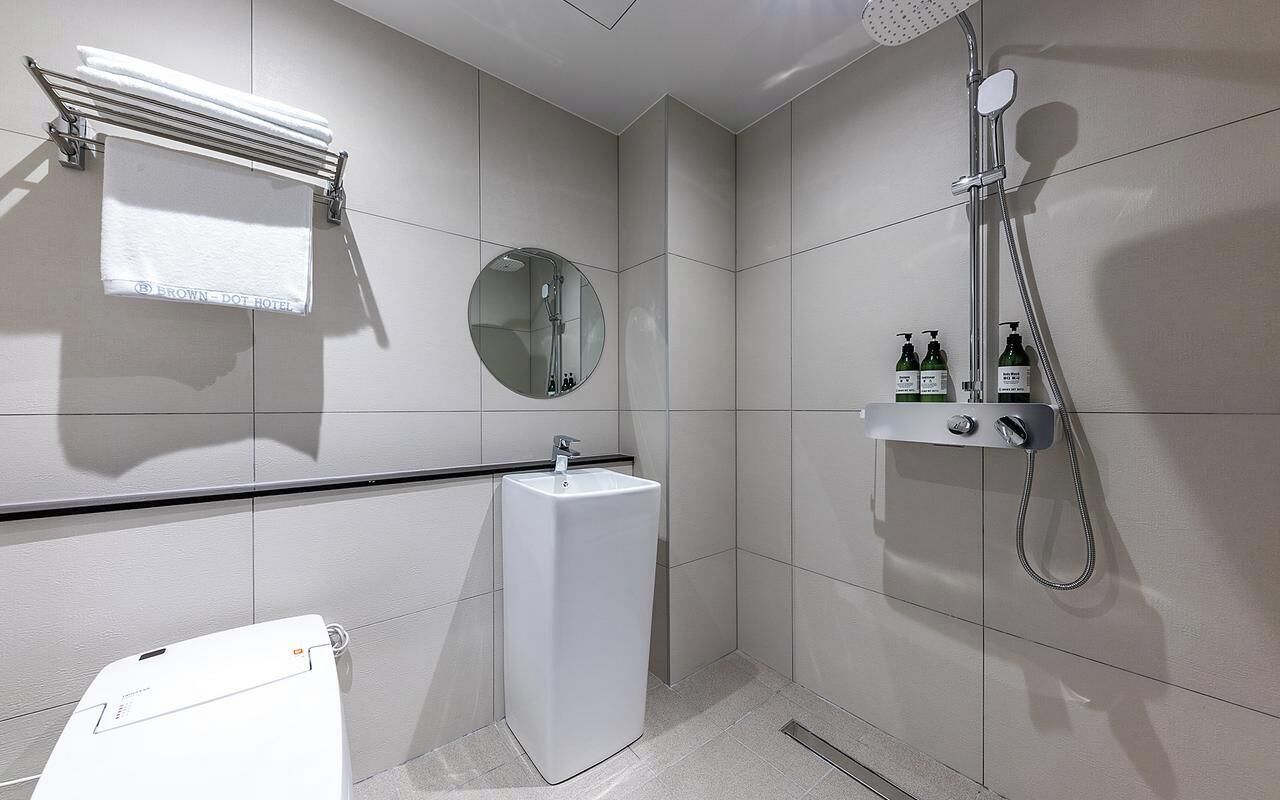A modern bathroom with a toilet, sink, mirror, towel rack, shower, and toiletries.