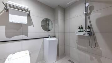 A modern bathroom with a toilet, sink, mirror, towel rack, shower, and toiletries.