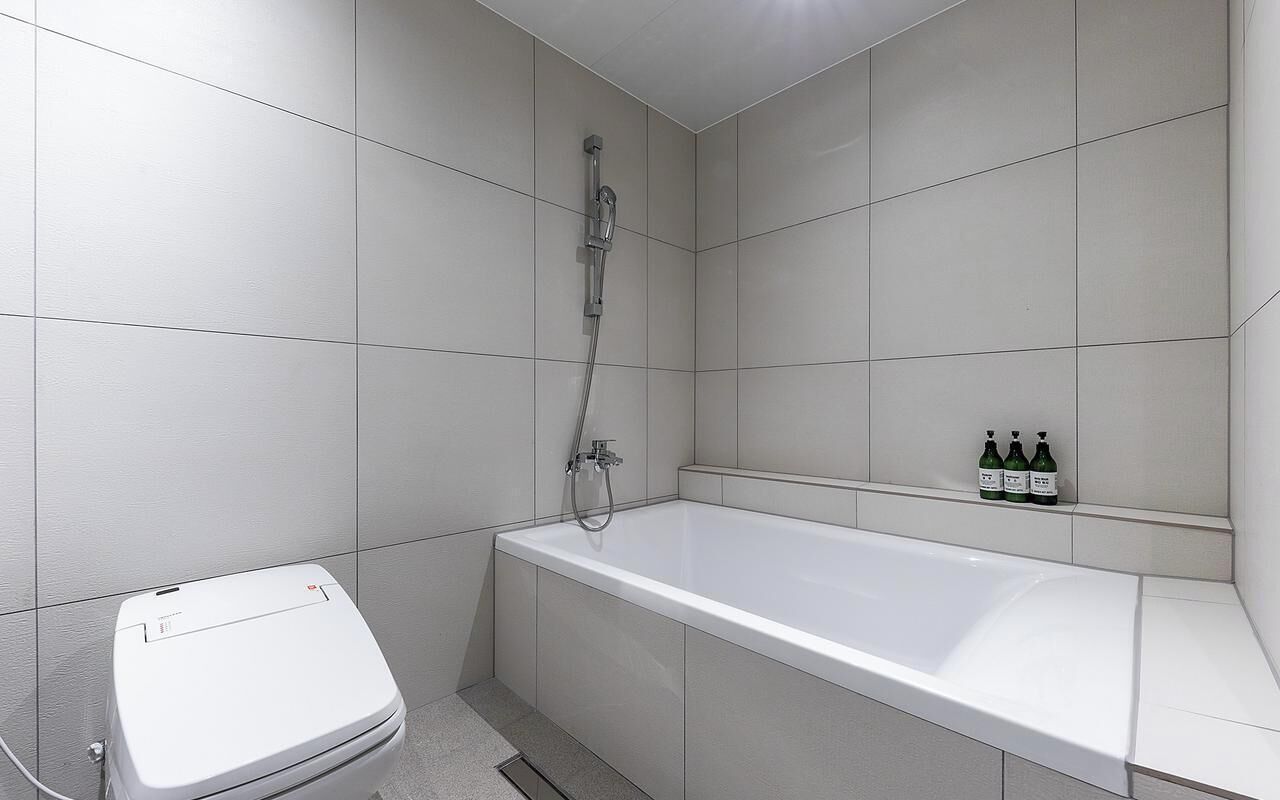 Ein Badezimmer mit Toilette, Badewanne und Dusche. Auf dem Regal stehen drei Flaschen.