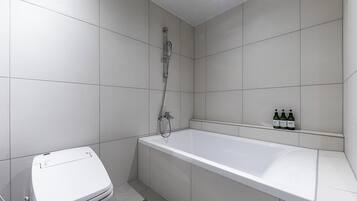 Une salle de bain avec des toilettes blanches, une baignoire et une douche. Il y a trois bouteilles sur l’étagère.
