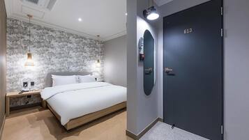 Una habitación de hotel moderna con cama, mesitas de noche, espejo montado en la pared y una puerta con número.