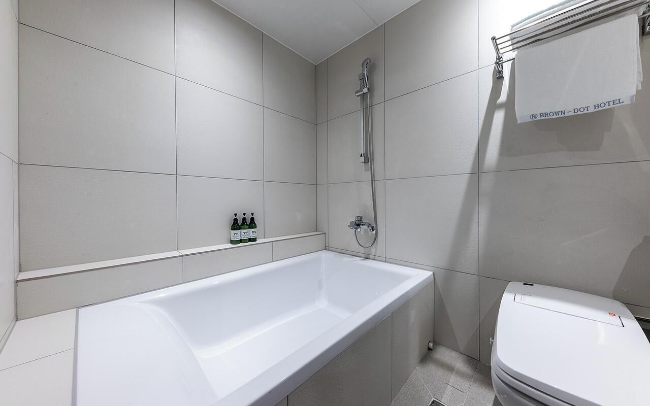 Une salle de bain moderne avec une baignoire, une douche et des toilettes. On peut voir des bouteilles de shampoing et d’après-shampoing accrochées au mur.