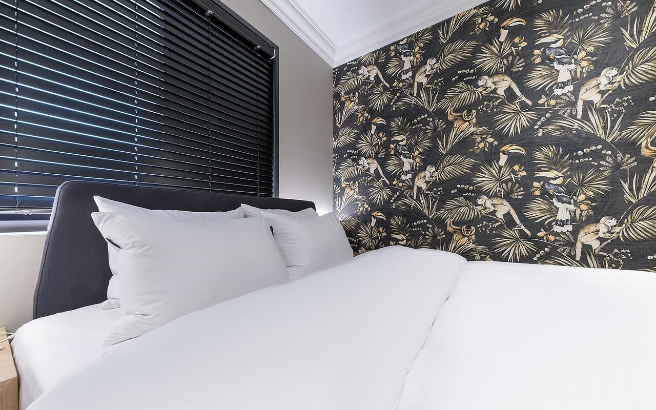 A bed with white bedding, a dark headboard, and a window with blinds.