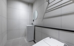Un baño moderno con azulejos blancos, un lavamanos, un espejo y una zona de ducha.