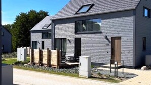 Ein modernes, zweistöckiges Haus mit geneigtem Dach, großen Fenstern und einer sichtbaren Satellitenschüssel.