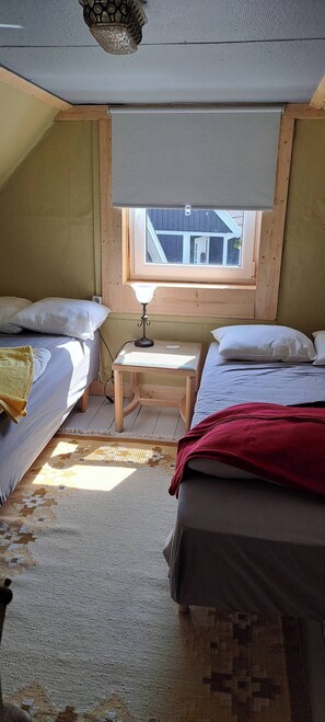 A small, cozy room with two beds, a small table, a window, and a ceiling light fixture. - Welcome to Lillstugan (Jämshög)
