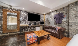 Una habitación con pared de piedra, un televisor de pantalla plana, un sofá de cuero, una mesa de centro de madera y una mesita con un hervidor.