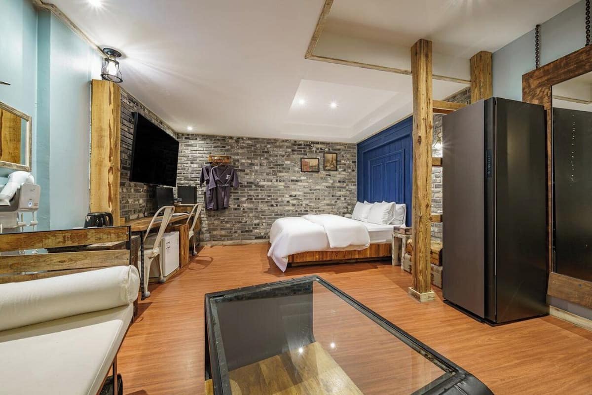 Una habitación de hotel con una cama, un escritorio con una silla, un espejo grande y un refrigerador.