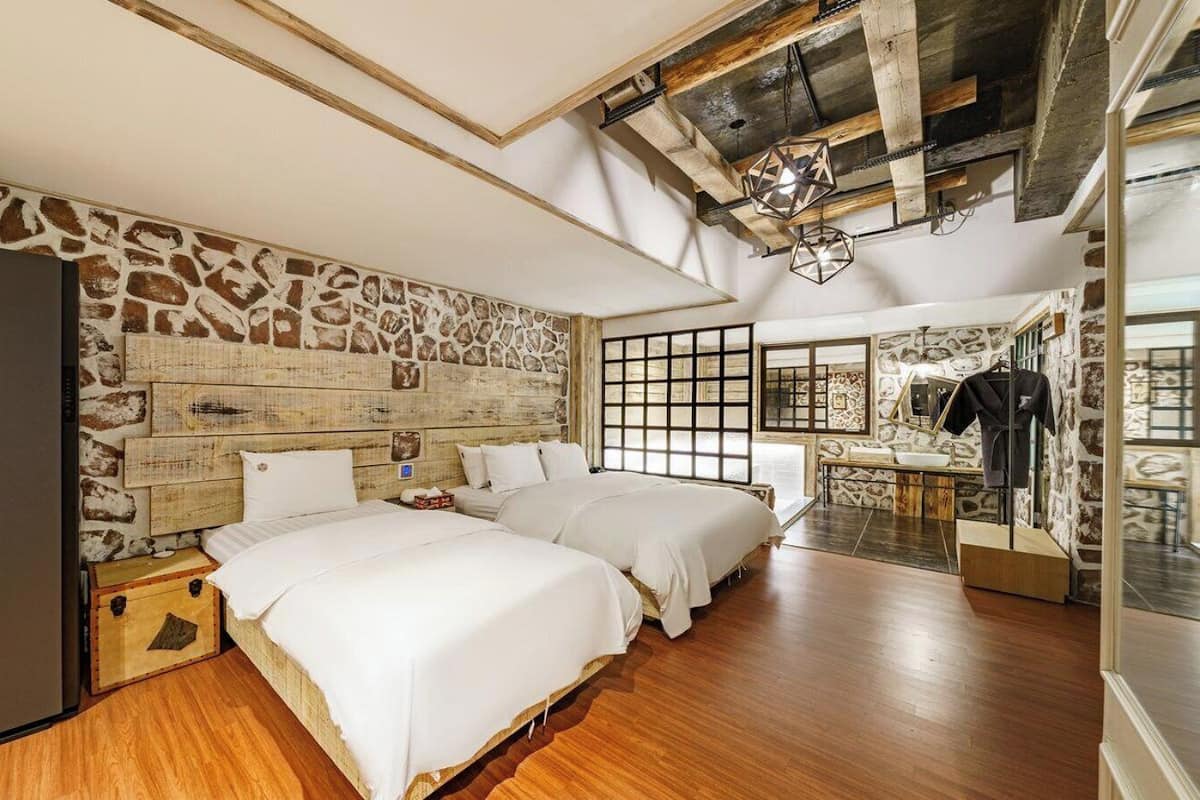 Un dormitorio con dos camas, una pared de piedra, suelo de madera y vistas a una zona de cocina.