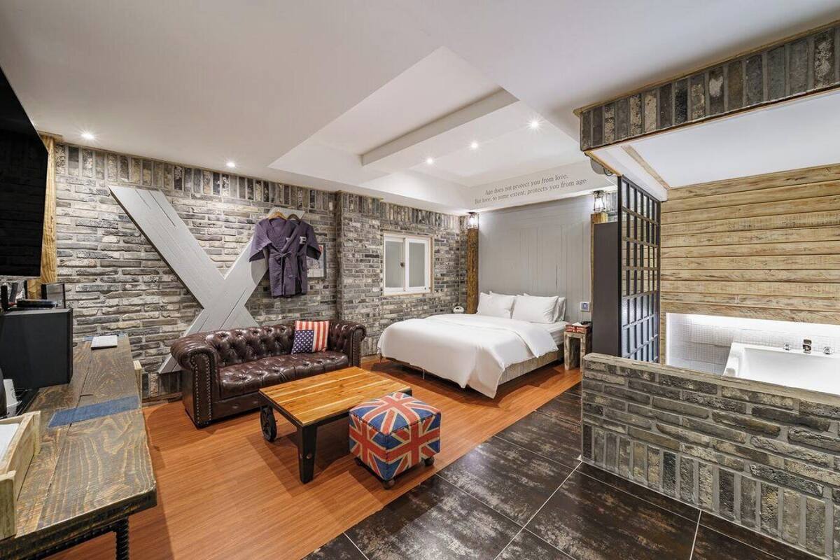 Una habitación de hotel moderna con pared de piedra, cama, sofá, mesa de centro y bañera.
