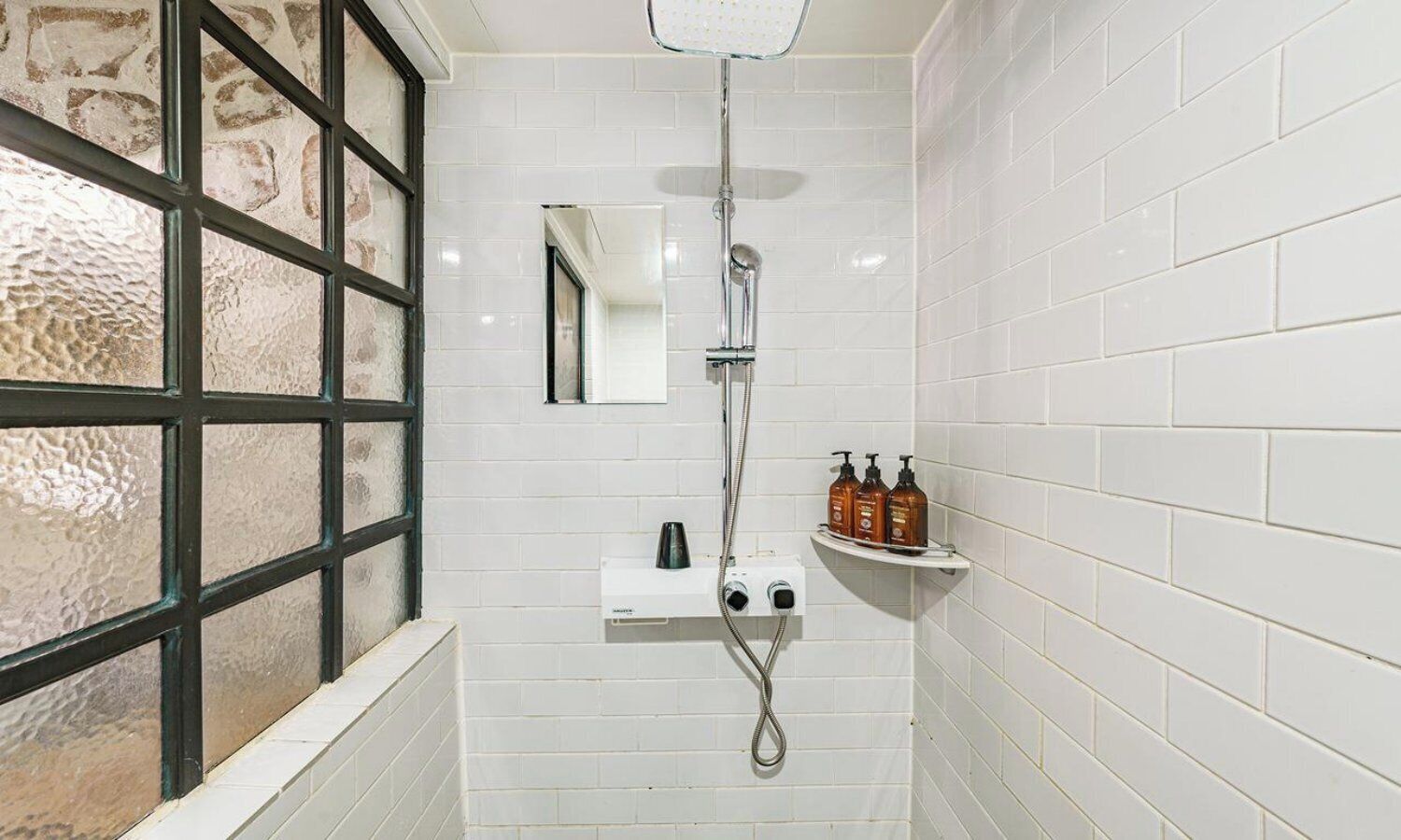 Un baño con ducha, espejo, lavamanos y ventana con vistas.