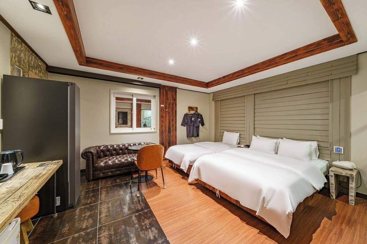 Una habitación de hotel con techo de madera, dos camas, un sofá, una mesita y un televisor.