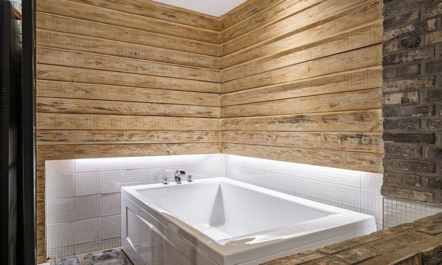 Un baño moderno con una bañera grande, paneles de madera y suelo de baldosas.