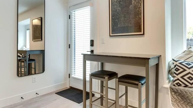 Een kamer met een grote spiegel, een tafel met twee krukken, een kunstwerk in een lijst aan de muur en een deur met zonwering.