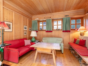 Interior acogedor de una cabaña con paredes de madera, un sofá rojo, un sofá verde a cuadros, una mesa de madera y una ventana con cortinas.