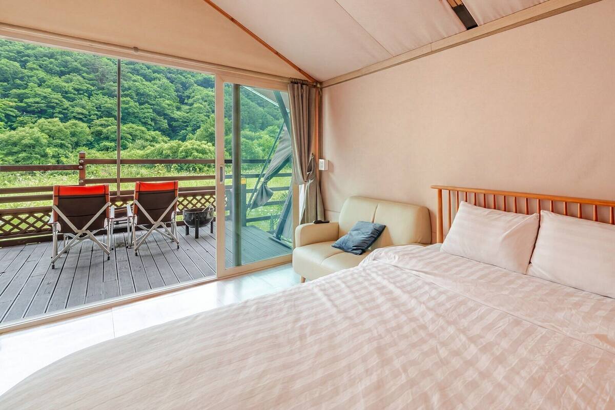 A bedroom with a large bed, a sofa, and a balcony with chairs.