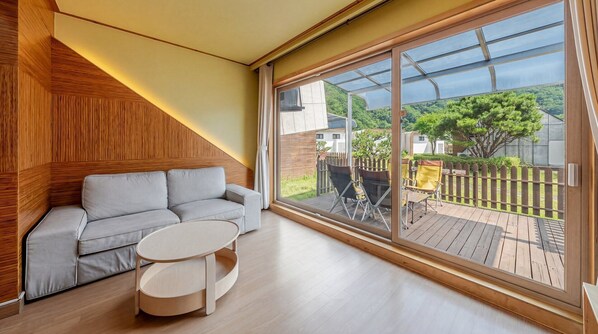 A modern living room with a sofa, a round coffee table, and a large sliding glass door leading to an outdoor deck. - Hongcheon Huttopia Glamping (Hongcheon)