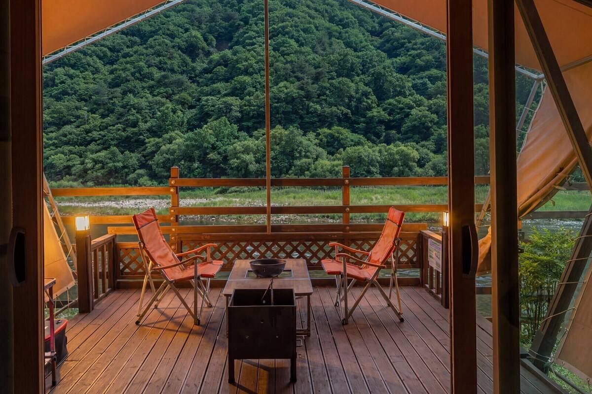A wooden deck with a table and chairs, overlooking a forested area.