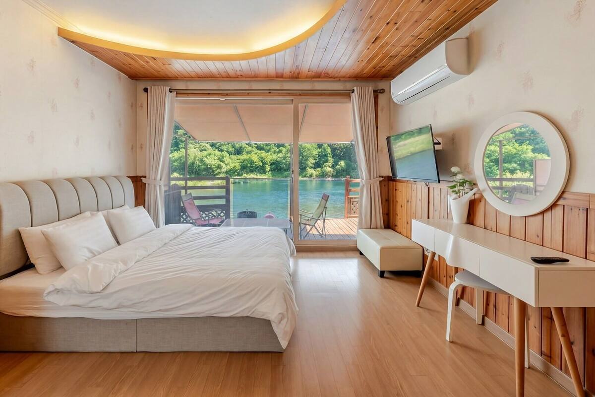 A bedroom with a bed, a TV, a desk, and a view of a lake.