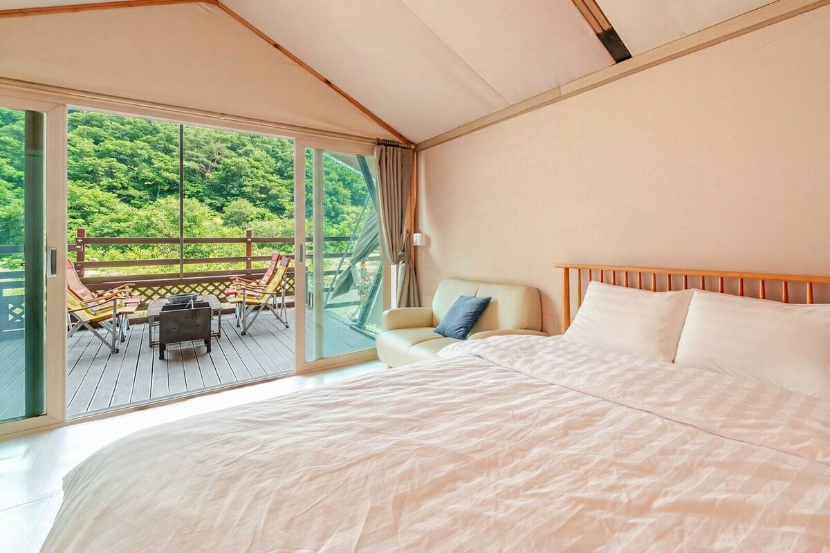 A bedroom with a large bed, a chair, and a view of a deck with chairs and a table.