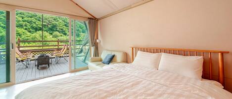 A bedroom with a large bed, a chair, and a view of a deck with chairs and a table.