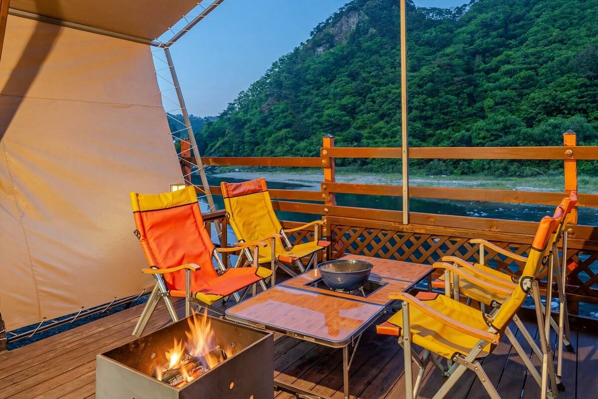 A deck with outdoor seating, a fire pit, and a view of a river and forest.