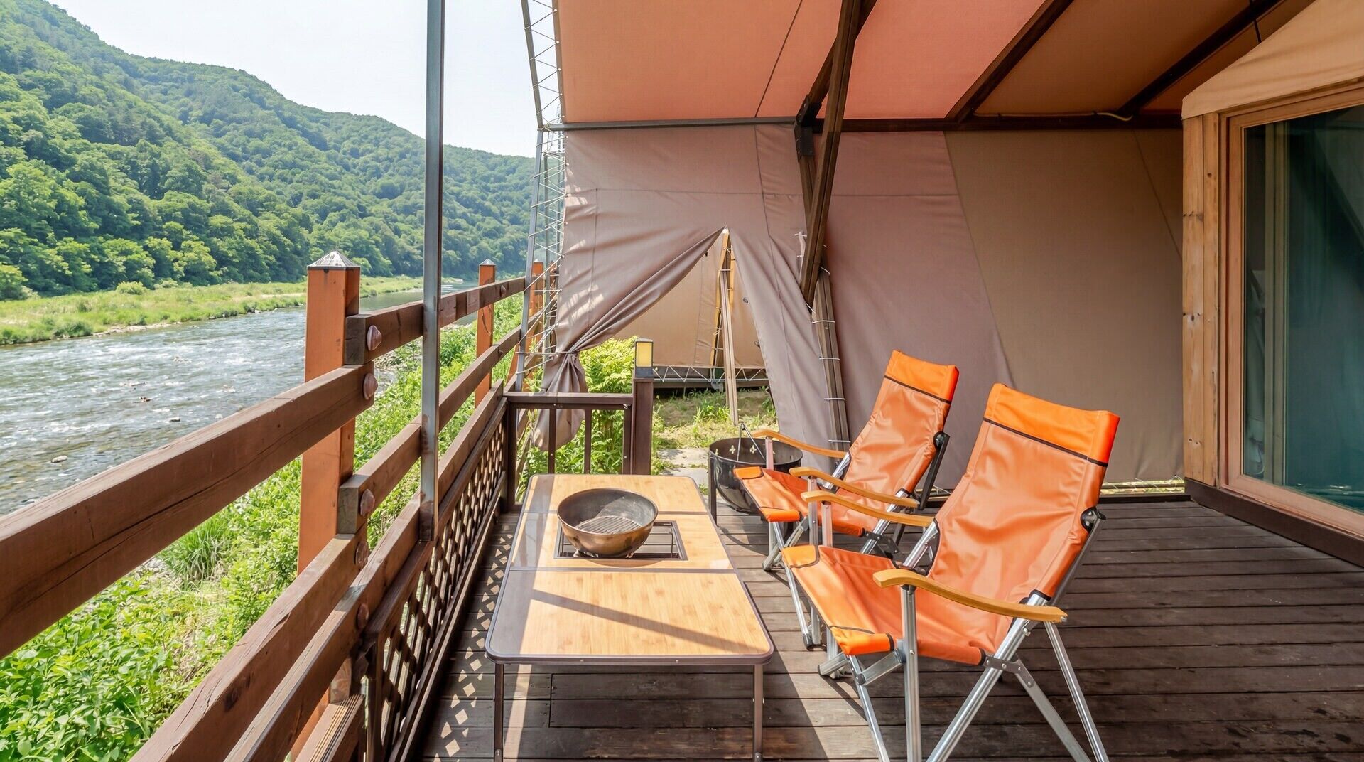 A deck with a table and chairs, overlooking a river and forested hills.