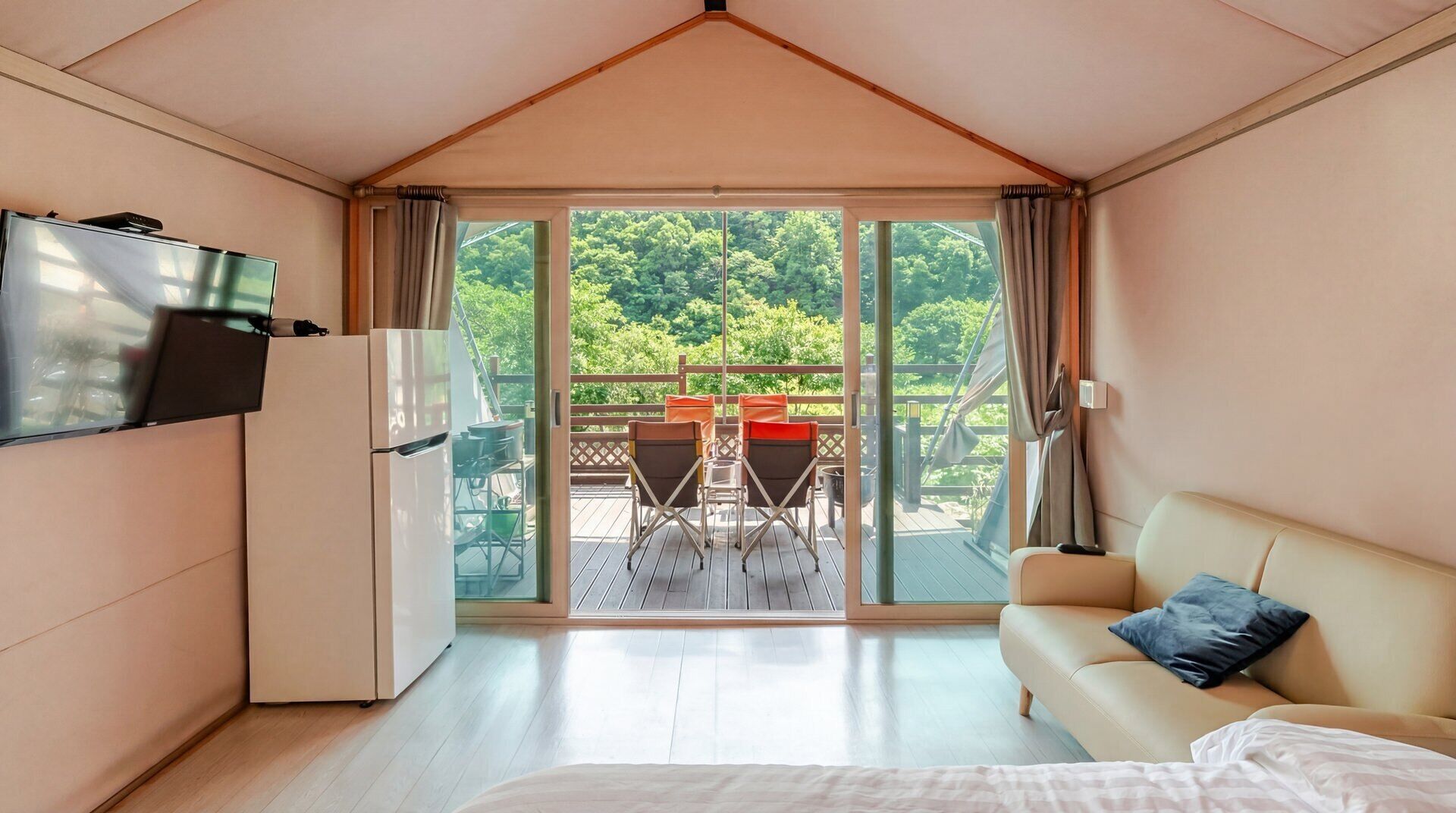 A room with a bed, a TV, a sofa, and a balcony with chairs and a table.