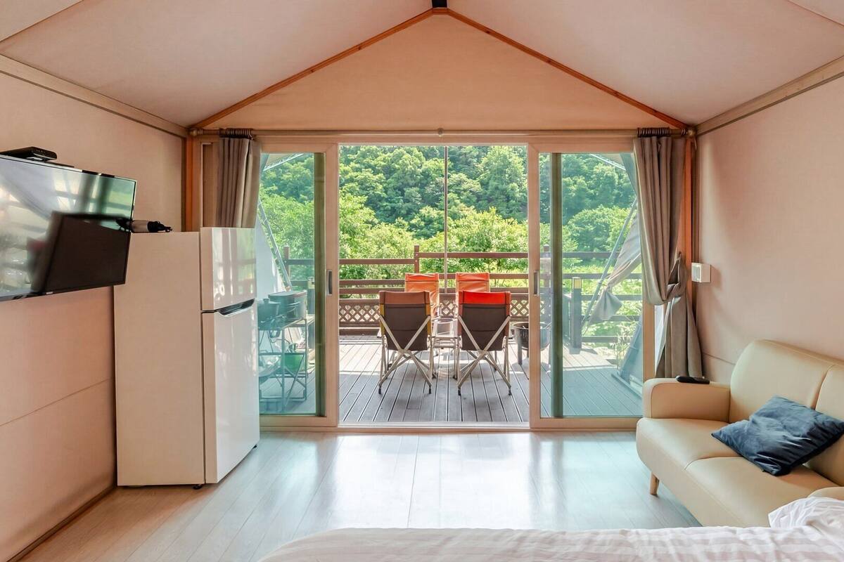 A room with a bed, a TV, a sofa, and a balcony with chairs and a table.