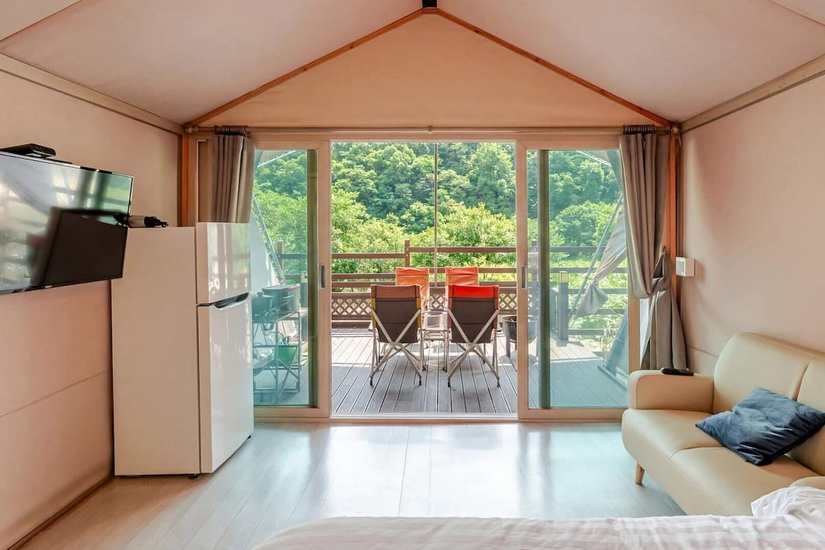 A room with a bed, a TV, a sofa, and a balcony with chairs and a table.