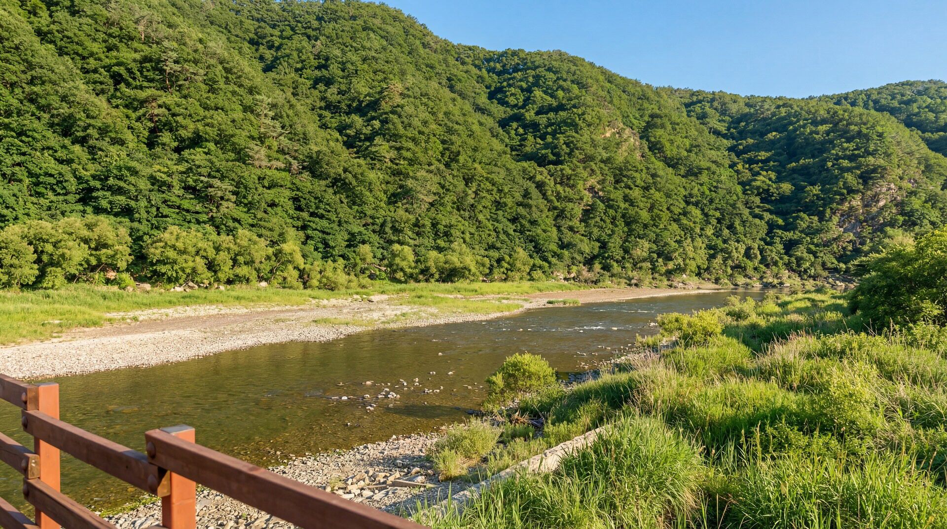 Ein Fluss mit einer Holzbrücke, umgeben von üppigen, grünen Hügeln.