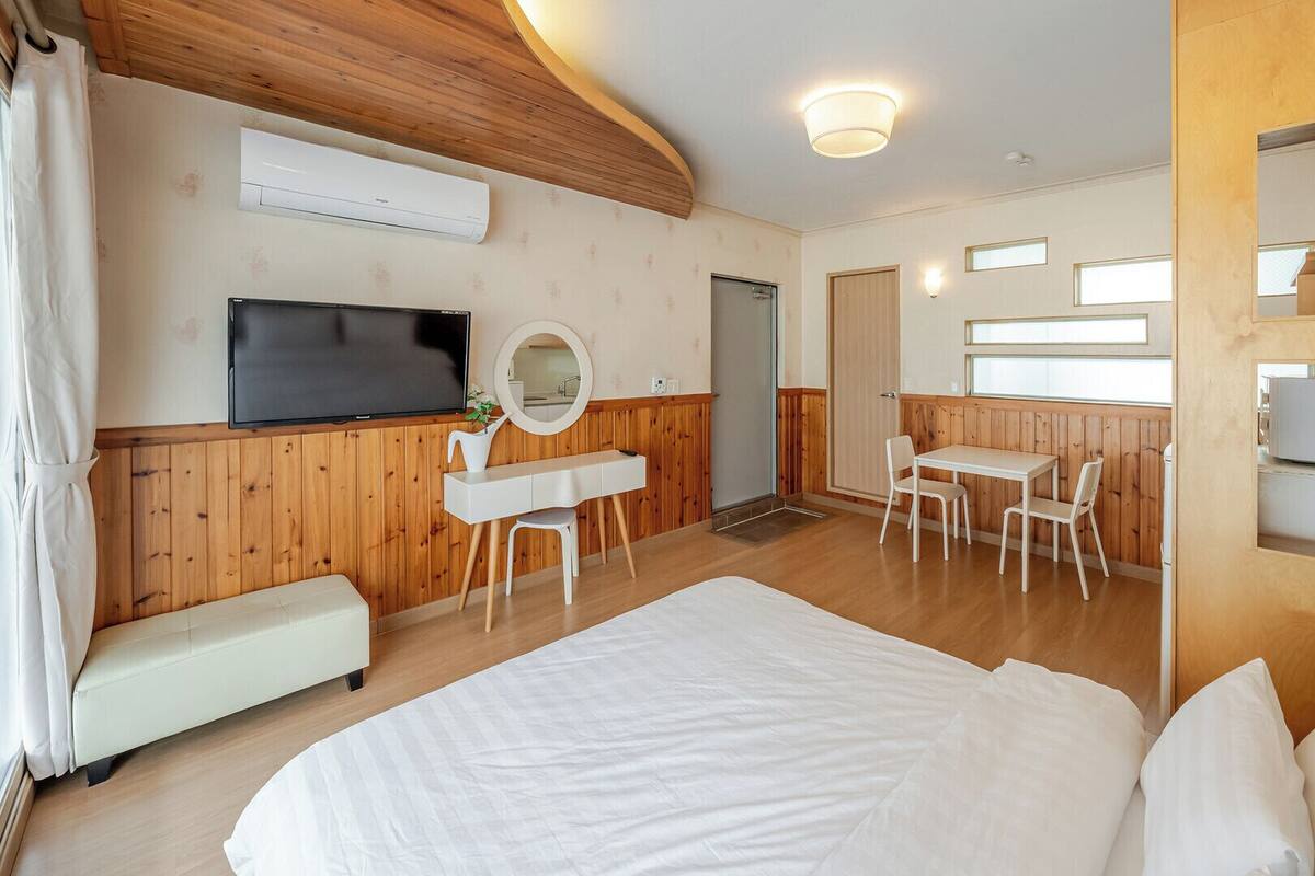 A hotel room with a bed, a TV, a desk with a chair, a small table with chairs, and a bathroom door.