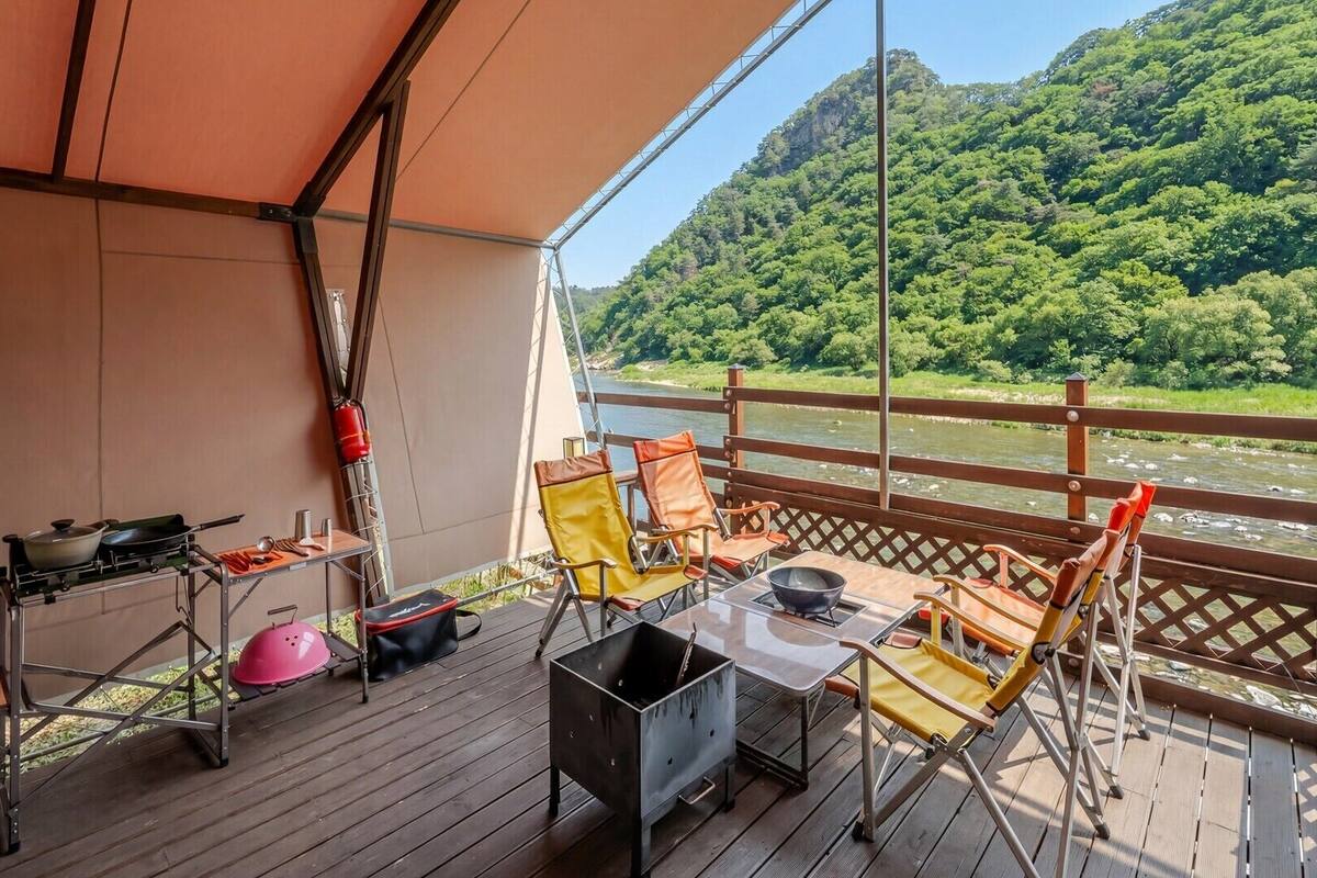 A deck with outdoor seating, a grill, and a view of a river and forest.