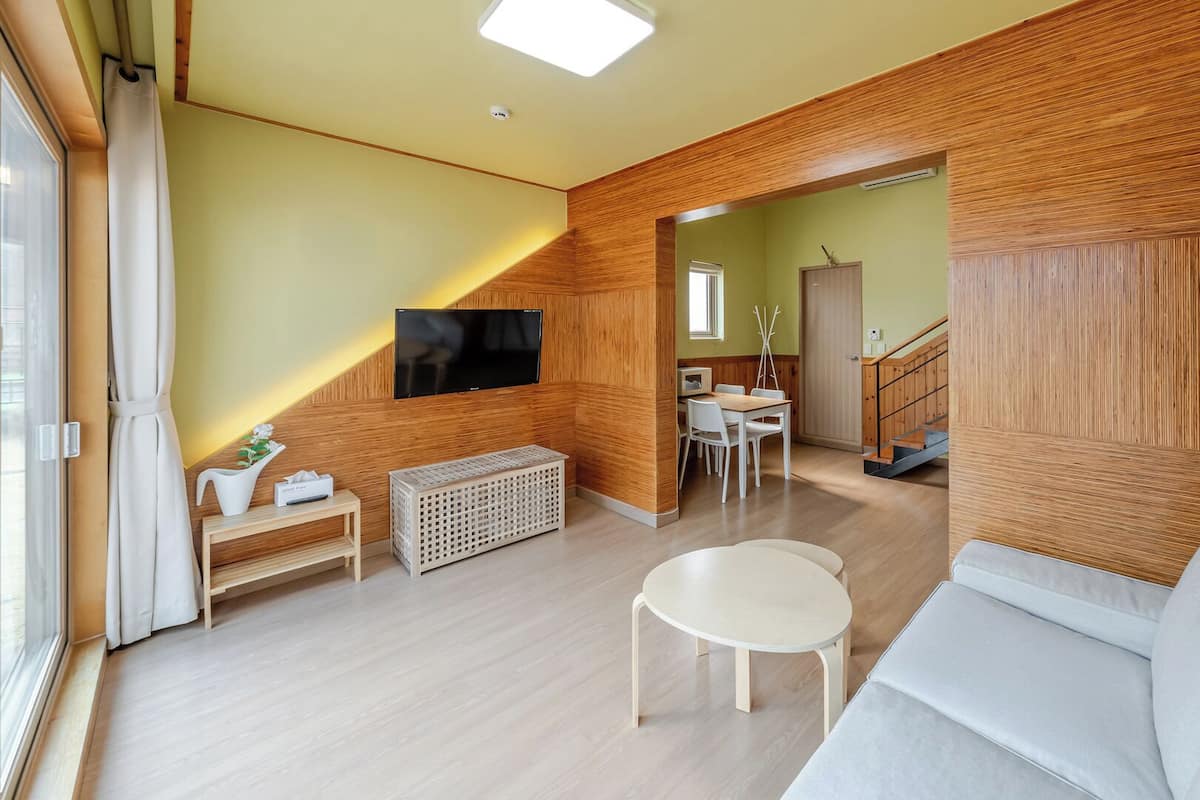 A modern living room with a TV, a sofa, a dining area, and a staircase.