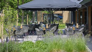 An outdoor seating area with tables and chairs, surrounded by greenery and a building in the background. - Cozy home in a holiday park with a swimming pool (Lage Mierde)