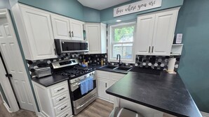 A kitchen with white cabinets, a stainless steel stove, a microwave, and a black countertop. - Freshly remodeled premium trailer in prime location! (Port Colborne)