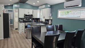 A modern kitchen with white cabinets, a black countertop, and a dining area with a table and chairs. - Freshly remodeled premium trailer in prime location! (Port Colborne)